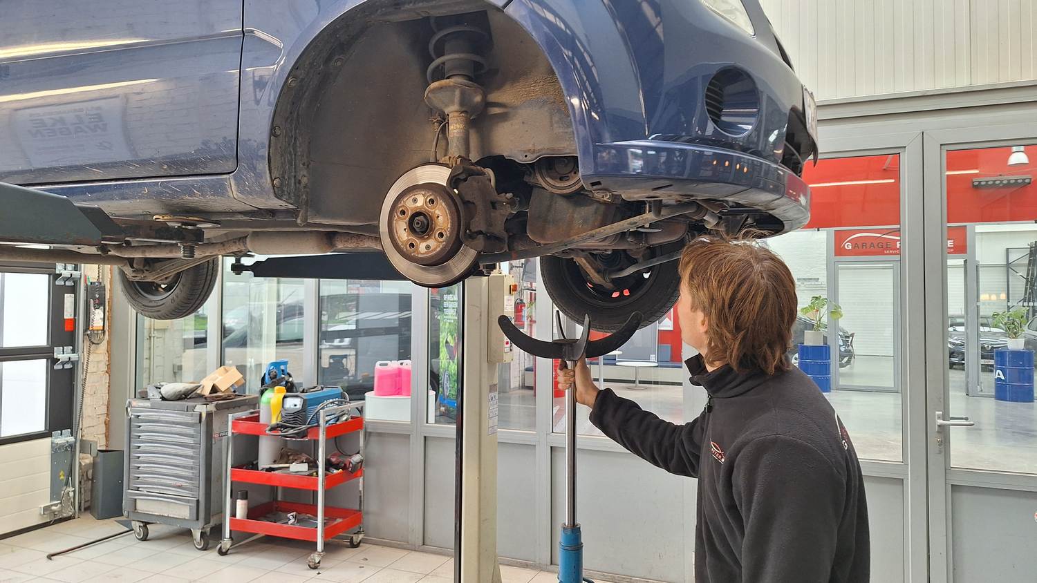 Thomas aan het werk aan een wagen op de hefbrug bij Garage Peter